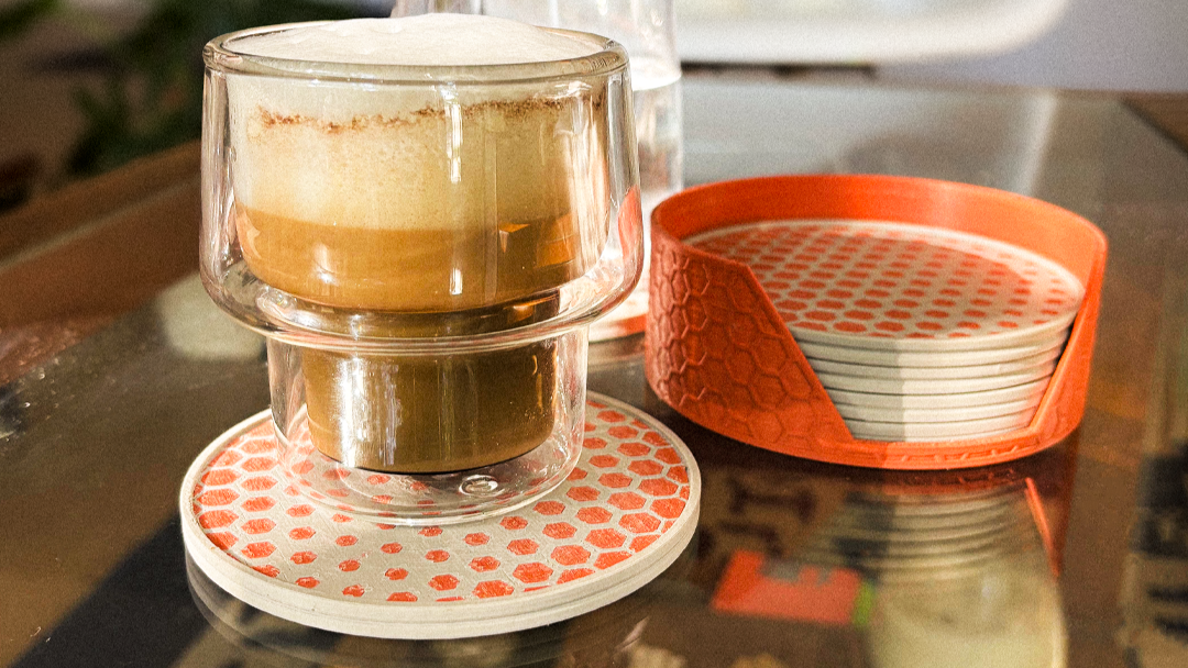 Stacked glass cups with a layered drink on a coaster, with a blurred indoor background.