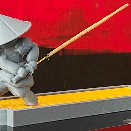 Sculpture of a person in traditional attire with an incense stick on a reflective surface against a red background